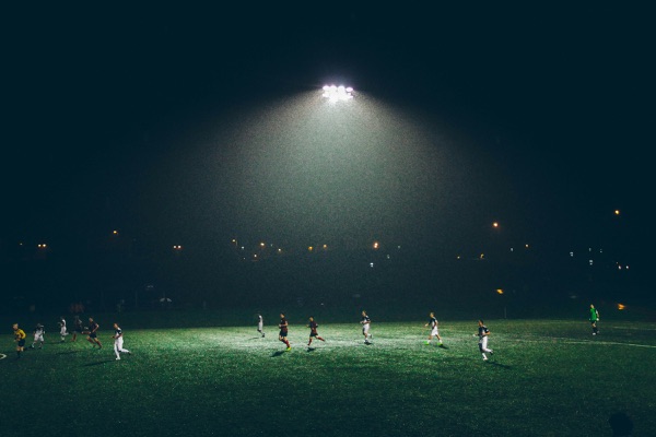 Soccer players running across a floodlit field during a night match
