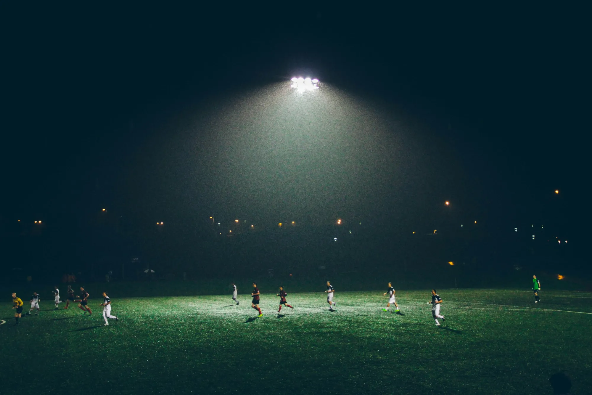 Soccer players running across a floodlit field during a night match