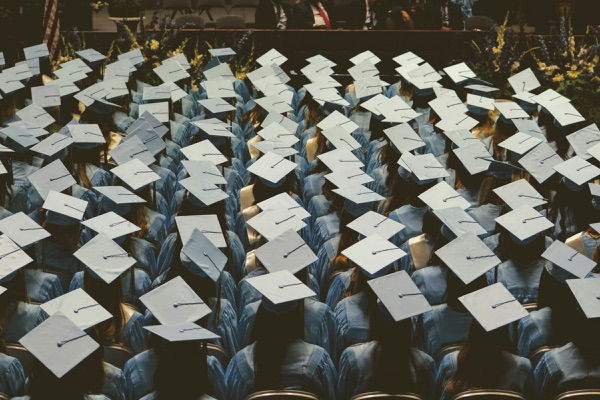 Rows of graduates in light blue caps and gowns seen from behind during a graduation ceremony